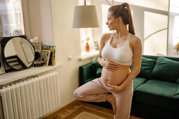 Těhotná žena cvičí jógu doma v obývacím pokoji.